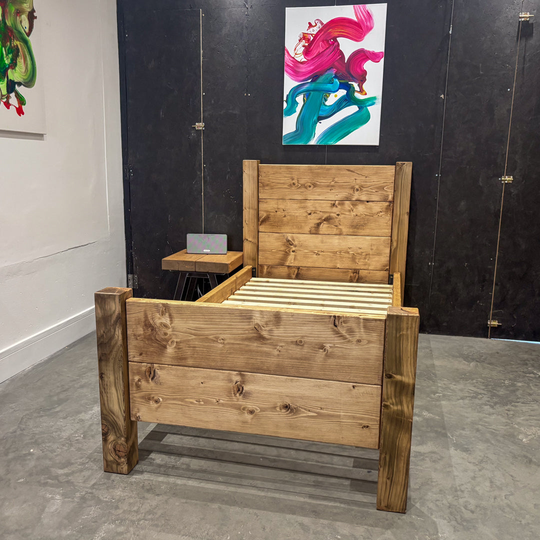 Handmade industrial-style chunky wooden single bed in a rustic bedroom setting