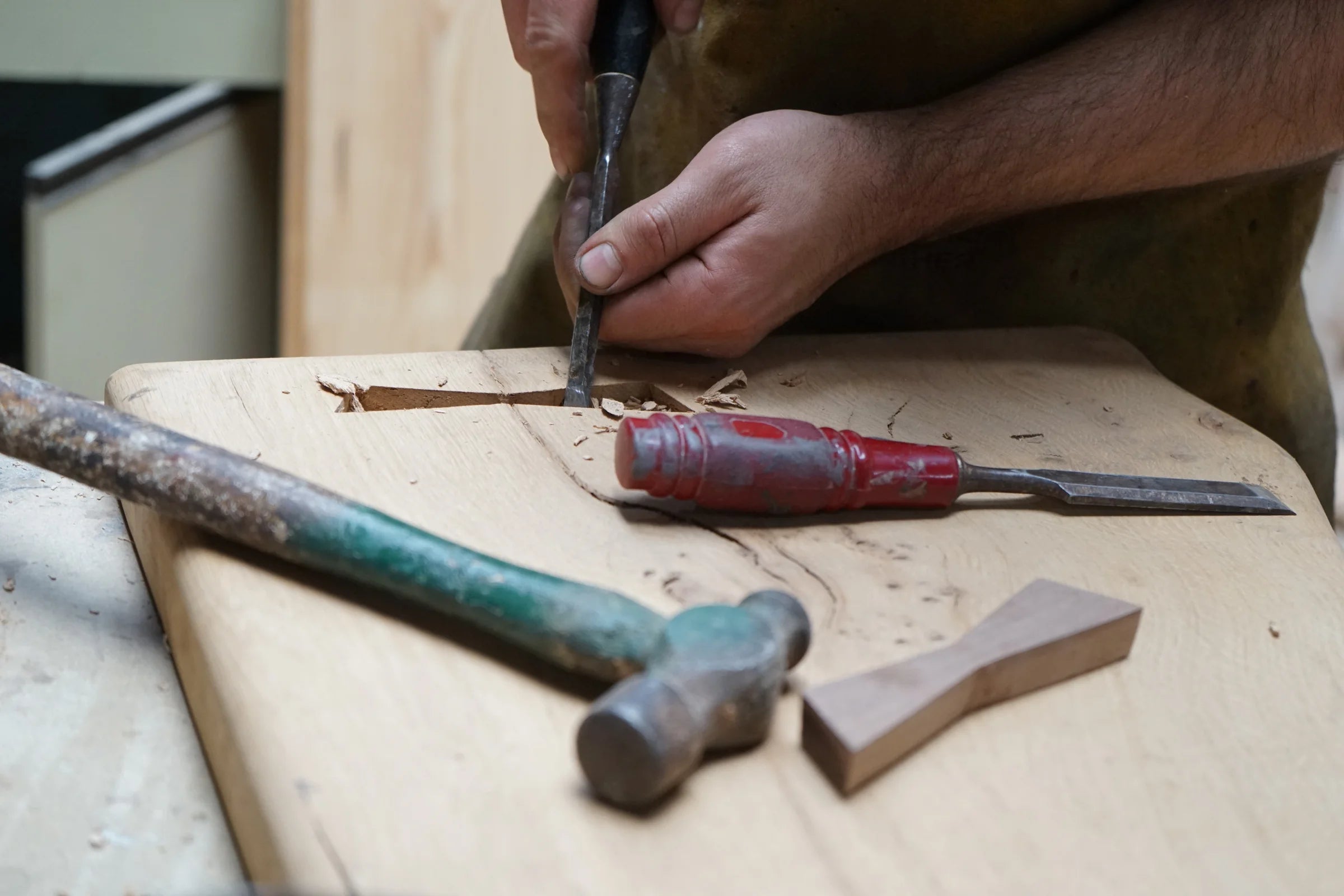 A detailed shot of a hardwood table being chizzled into shape with a hammer in the foreground