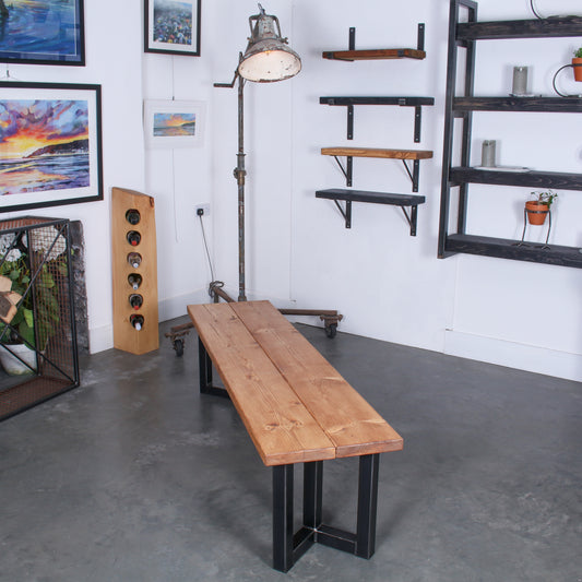 Extra Chunky Chunk Three bench in a rustic industrial setting. Features inverted triple V shaped legs and a farmhouse stain.