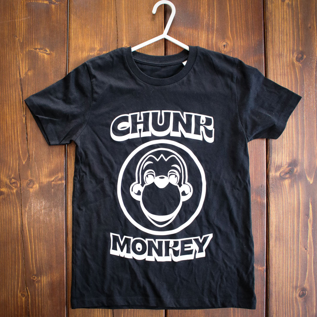 Front of black children’s t-shirt with Chunk Monkey logo and text, displayed on rustic wooden surface