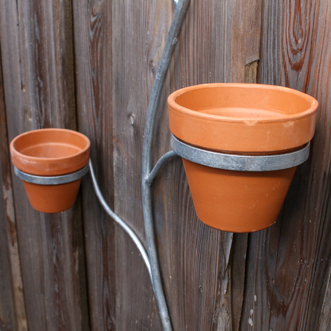Two terracotta pots attached to a metal strip against a wooden background