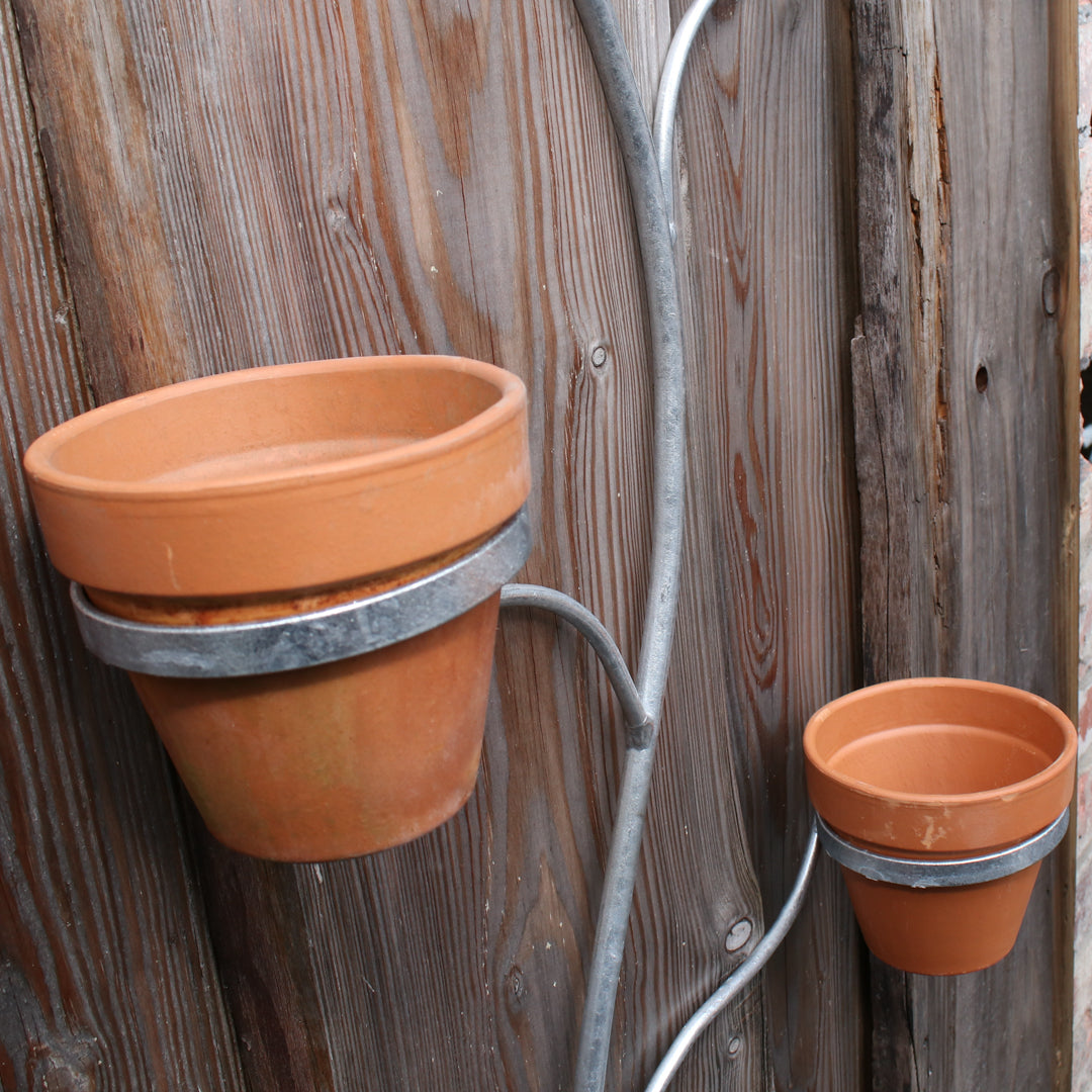 Two terracotta pots attached to a metal hook against a wooden fence.