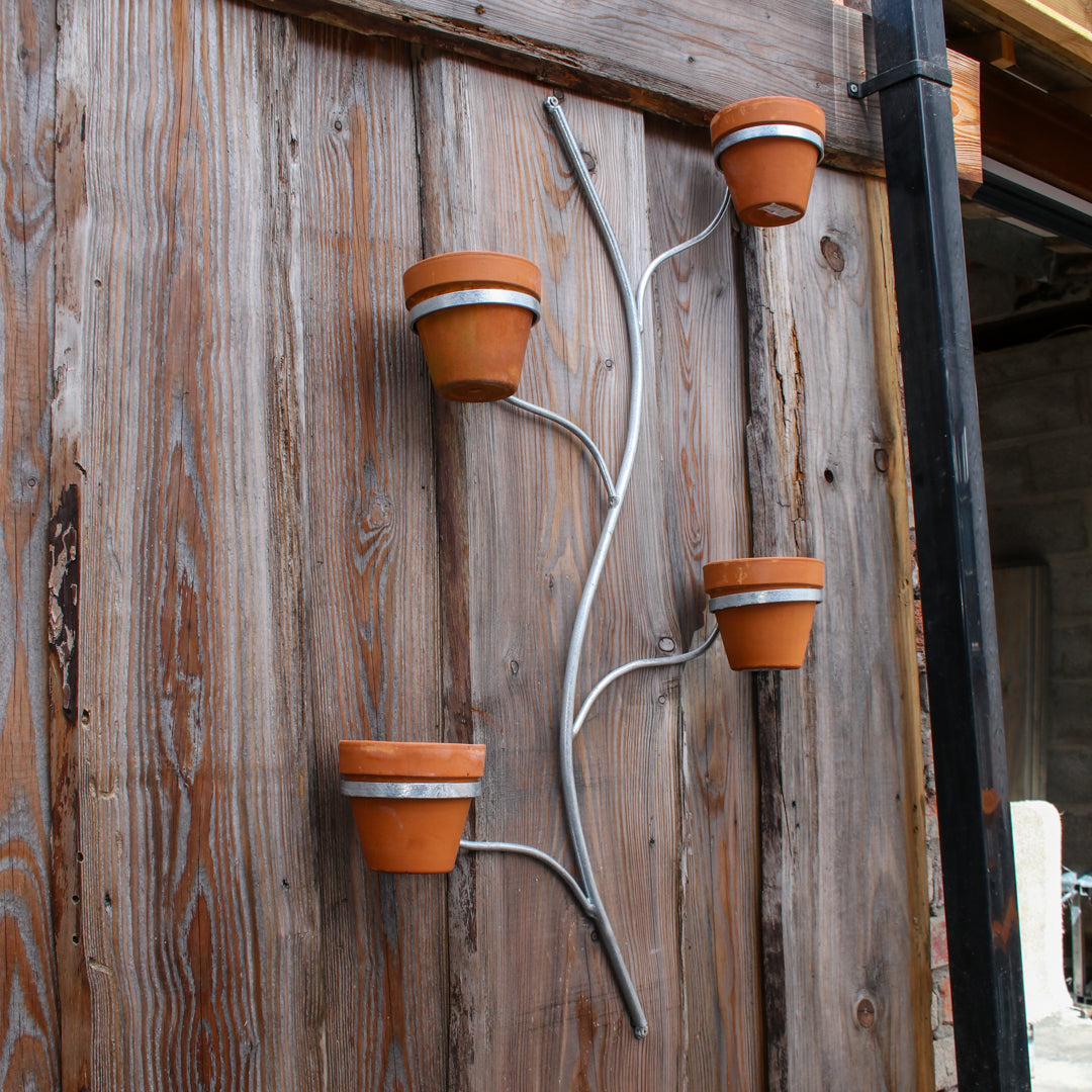 Decorative wall-mounted plant holder with terracotta pots on a wooden wall.