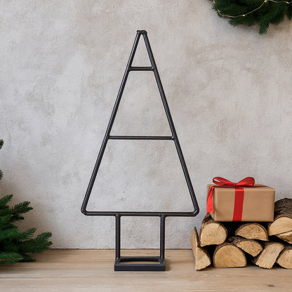 Black metal Christmas tree decoration on a wooden floor with logs and a gift box.